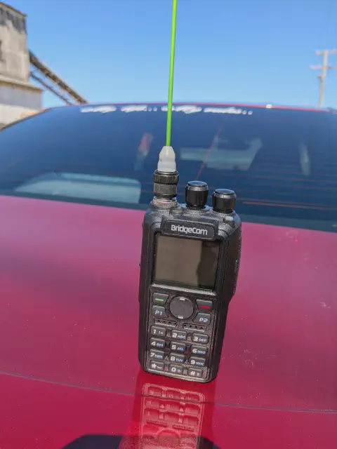 bridgecom maverick front view with green signal stick antenna attached black textured body two control knobs lcd display control buttons numeric keypad